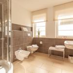 Badezimmer mit Dusche, Waschbecken, Toilette und Fenstern.