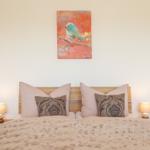 Ein Bett mit Kissen und Decke. An der Wand hängt ein Bild mit einem Vogel.