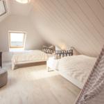 Zwei Betten unter Dachschrägen mit Fenster und Sitzgelegenheit.