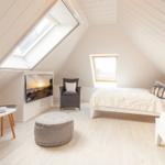 Dachgeschosszimmer mit Bett, Sessel, TV und Dachfenster.