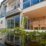 Haus mit Balkon, Terrasse und Teich im Vordergrund.
