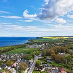 Panoramablick auf Küstenstadt mit grünen Feldern und blauem Meer unter strahlendem Himmel.