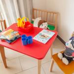 Rotes Kindertisch mit Stühlen, Spielzeug und Büchern. Fenster mit Blick auf Garten.