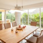 Essbereich mit Holztisch und braunen Stühlen, großes Fenster zur Terrasse und Garten.