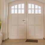 Haus-Eingang mit weißen Doppeltüren und einem weißen Vase mit Pflanzen.