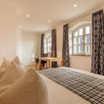 Schlafzimmer mit Bett, Schreibtisch und Fenster mit Vorhängen.