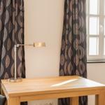 Holztisch mit Lampe zwischen zwei Fenstern mit Vorhängen.