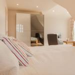 Schlafzimmer mit Bett, Spiegelschrank und Sitzgelegenheiten unter Dachschrägen.