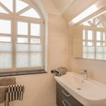 Badezimmer mit Waschbecken, Spiegel und großem Fenster mit Jalousien.