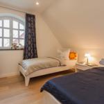 Zwei Betten mit Kissen und Decken, Fenster mit Vorhängen und Nachttisch mit Lampe.