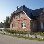 Rotes Backsteinhaus mit dunklem Dach und weißen Fenstern an einer Straße.