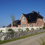 Haus mit rotem Ziegelstein, weißem Zaun und Steinmauer an Straße