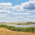 Weitläufiger See mit grünen Uferzonen und bewölktem Himmel.