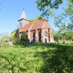 Roter Backsteinbau mit Turm und Friedhof. Gras und Bäume umgeben das Gebäude.