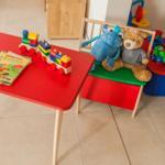Roter Kindertisch mit Buch und Zug. Hocker mit Plüschtieren und Spielzeugkasten.