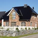 Zweistöckiges Haus mit Backsteinfassade und dunklem Dach hinter weißem Zaun.