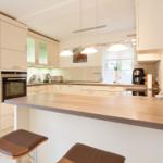 Moderne Küche mit Holzoberfläche und integriertem Herd. Barhocker und Fenster sichtbar.