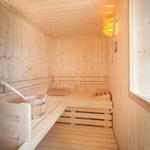 Holzsauna mit Sitzbänken, Eimer und warmem Licht an der Wand.