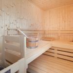 Sauna mit Holzbank und Eimer. Holzwände und -boden. Drei Sitzstufen.