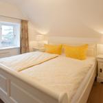 Schlafzimmer mit weißem Bett, gelben Kissen und Nachttischen mit Lampen.