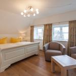 Schlafzimmer mit Bett, Sitzgelegenheiten und Fenstern mit Vorhängen.