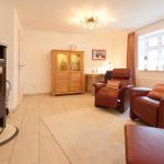 Wohnzimmer mit Kamin, zwei Ledersessel und Holzschrank.