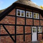 Haus mit strohgedecktem Dach, roten Ziegeln und weißen Fenstern.