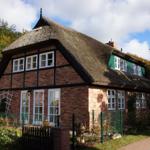 Rotes Backsteinhaus mit Strohdach und grünen Fensterläden.