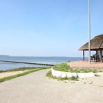 Haus mit Dach aus Stroh, Terrasse und Blick auf Wasser und Steg.