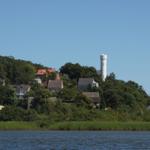 Wohnhäuser und ein weißer Turm auf einer bewaldeten Insel am See.
