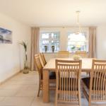 Esszimmer mit Holztisch, Stühlen und Fenstern. Wandbild und Deckenleuchte.