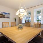 Esszimmer mit Holztisch, Stühlen und Fenster. Deckenleuchte und Wandbild sichtbar.