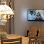 Esstisch mit Holzstühlen und Pendelleuchte. Fernseher an der Wand.