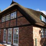 Haus mit strohgedecktem Dach, roten Ziegeln und weißen Fenstern.