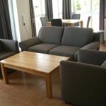 Wohnzimmer mit Sofa, Sessel und Holztisch. Küche und Essbereich im Hintergrund.