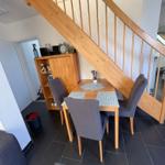 Essbereich mit Tisch, Stühlen und Holztreppe. Helle Wände und dunkler Boden.