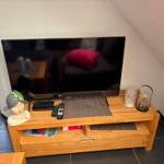 Flachbildfernseher auf Holz-TV-Schrank mit Dekoration und Fernbedienungen.