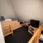 Ein Schlafzimmer mit Dachschräge, Bett, Stuhl und Fernseher.