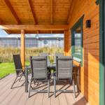 Terrasse mit Tisch und Stühlen neben Holzhäusern mit grünen Fensterrahmen.