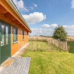 Holzhaus mit grüner Tür und Rasenfläche. Im Hintergrund Feld und Baum.