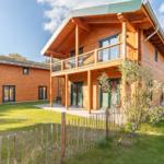 Holzhaus mit Balkon, Terrasse und Garten. Grünfläche und Zaun im Vordergrund.