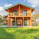 Holzhaus mit Balkon, Terrasse und Garten. Grüne Dachfläche und umliegende Bäume.