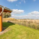 Holzhaus mit Garten und Blick auf Felder unter blauem Himmel.