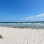 Weiterer Strand mit feinem Sand und tiefblauem Meer unter klarem Himmel.
