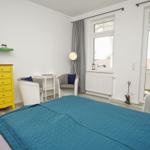 Schlafzimmer mit Bett, Schrank und Sitzgelegenheiten. Balkon mit Blick auf Felder.