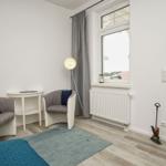 Zimmer mit zwei Sesseln, Tisch, Stehlampe und Blick auf Balkon.