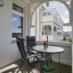 Terrasse mit Tisch und zwei Stühlen, Blick auf weiße Veranda und Straße.