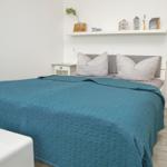 Schlafzimmer mit Bett, Nachttisch und Wandregal. Durchgang zur Wohnfläche.