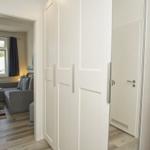 Hallenflur mit weißen Schränken und Blick in Wohnbereich mit Sofa und Fenster.