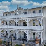 Zweistöckiges Haus mit weißen Balkonen und Terrasse. Gartenbereich mit Sitzgelegenheiten.